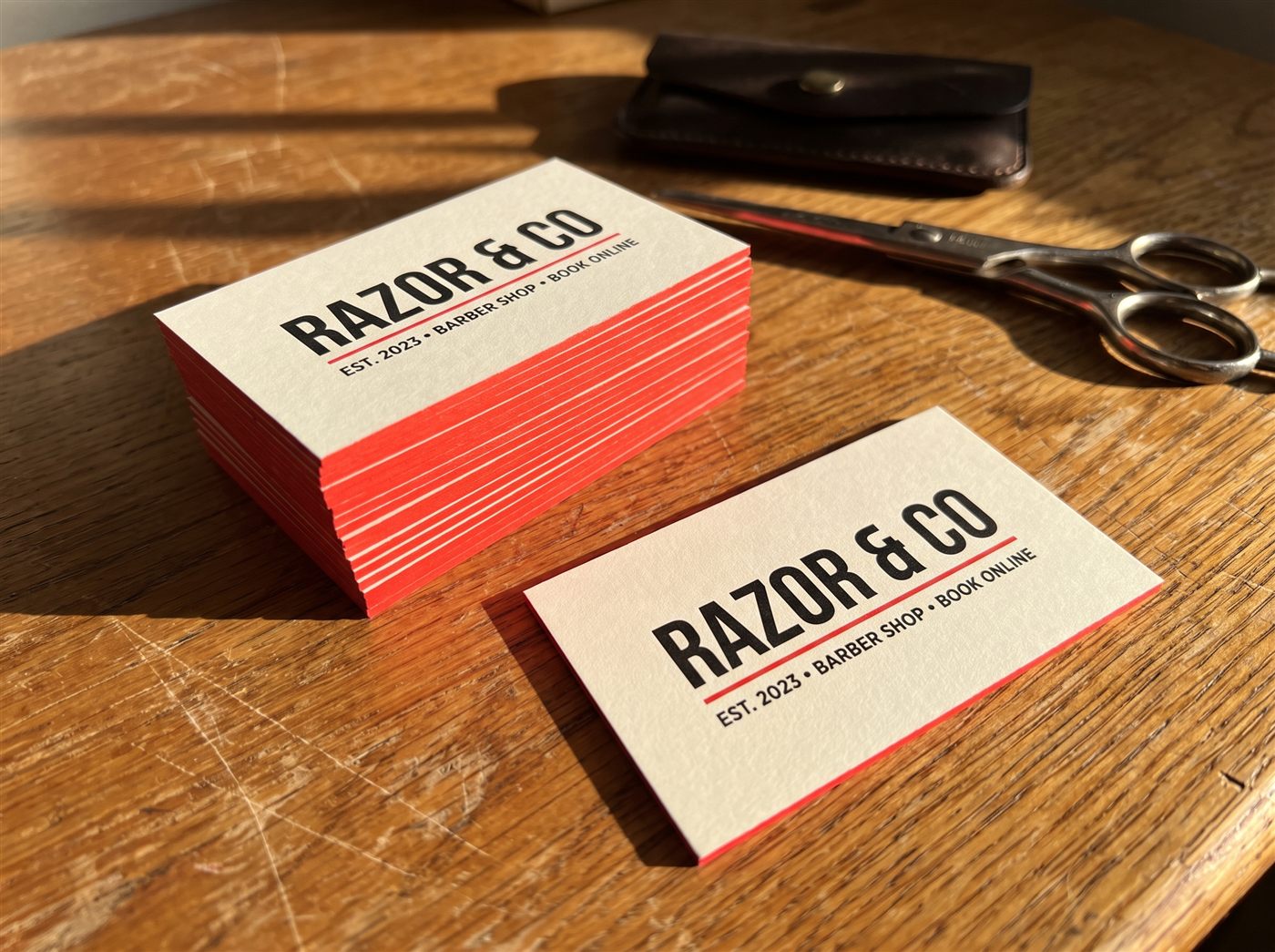 A stack of ultra-thick business cards with a bright red painted edge on a sunlit oak desk