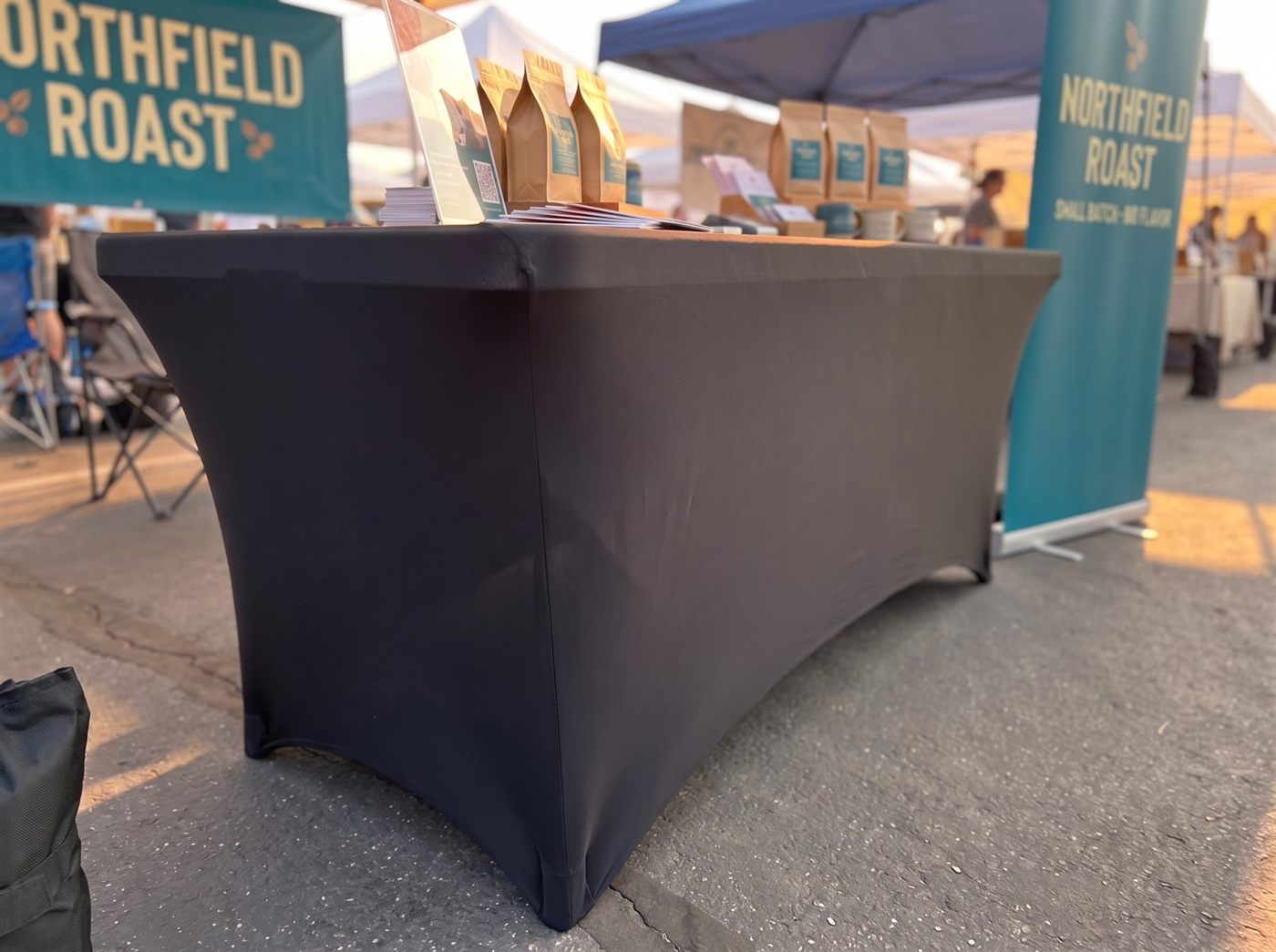 The plain black stretch table cover pulled taut over the six-foot table, corners crisp and sides curving under