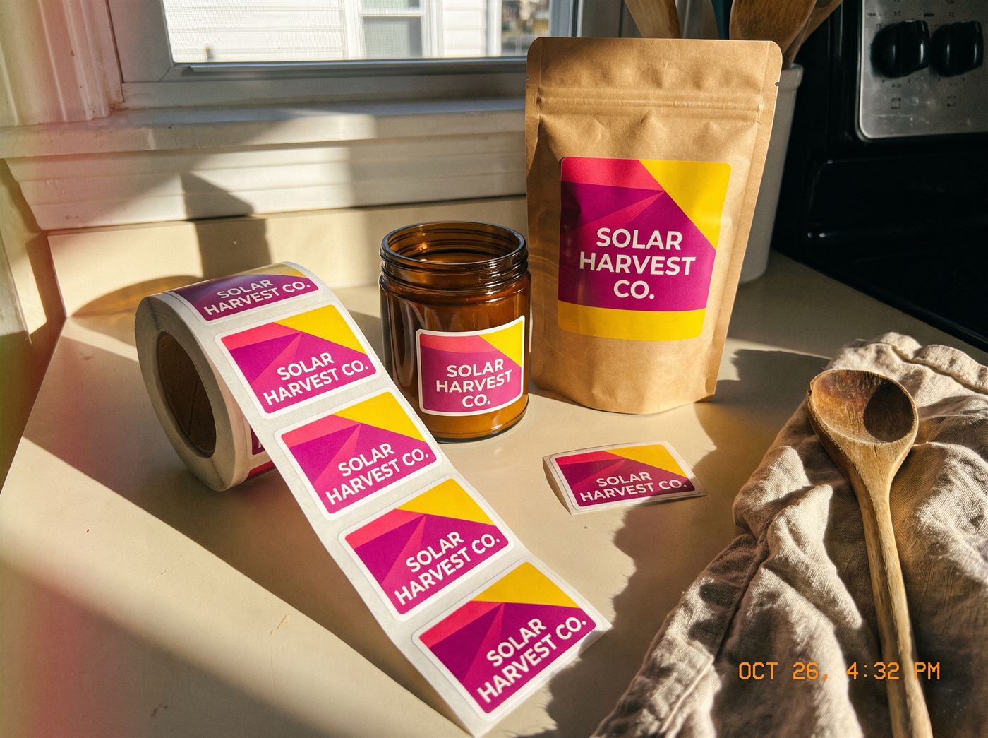 Roll of bright die-cut product labels unrolled on a kitchen counter next to a labeled amber jar and kraft pouch