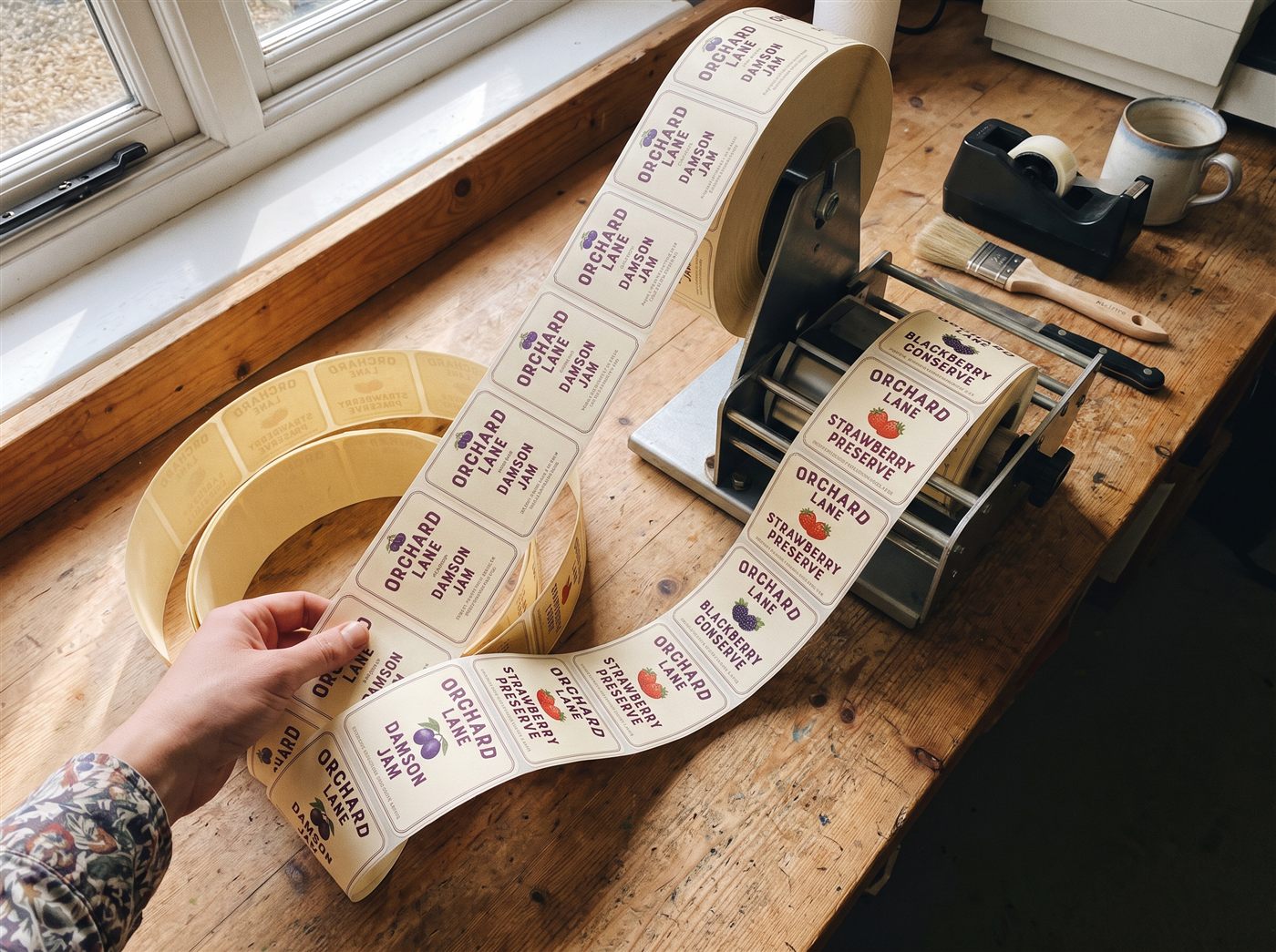 A large roll of printed paper labels unspooling toward a tabletop applicator